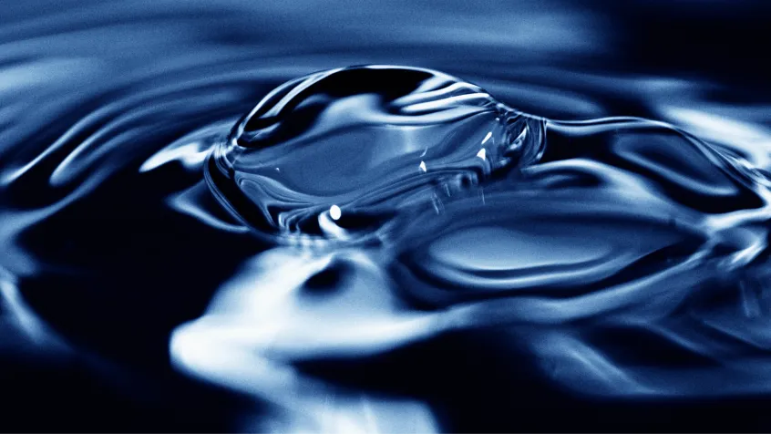 Close-up of a droplet creating ripples on dark blue water surface.