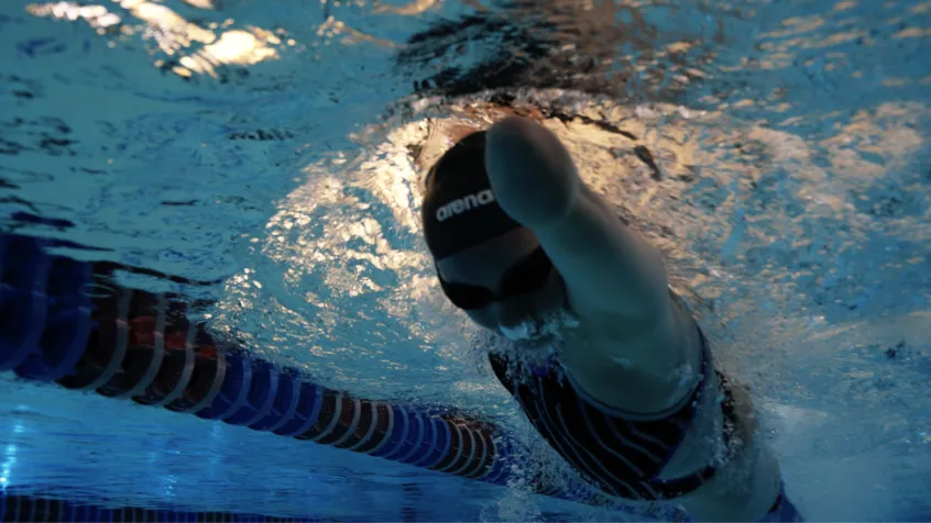 Swimmer wearing a black swim cap and goggles performing a freestyle stroke underwater near lane dividers in a pool.