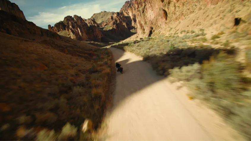 Motorcycle riding on a dirt road winding through a rocky desert canyon landscape.
