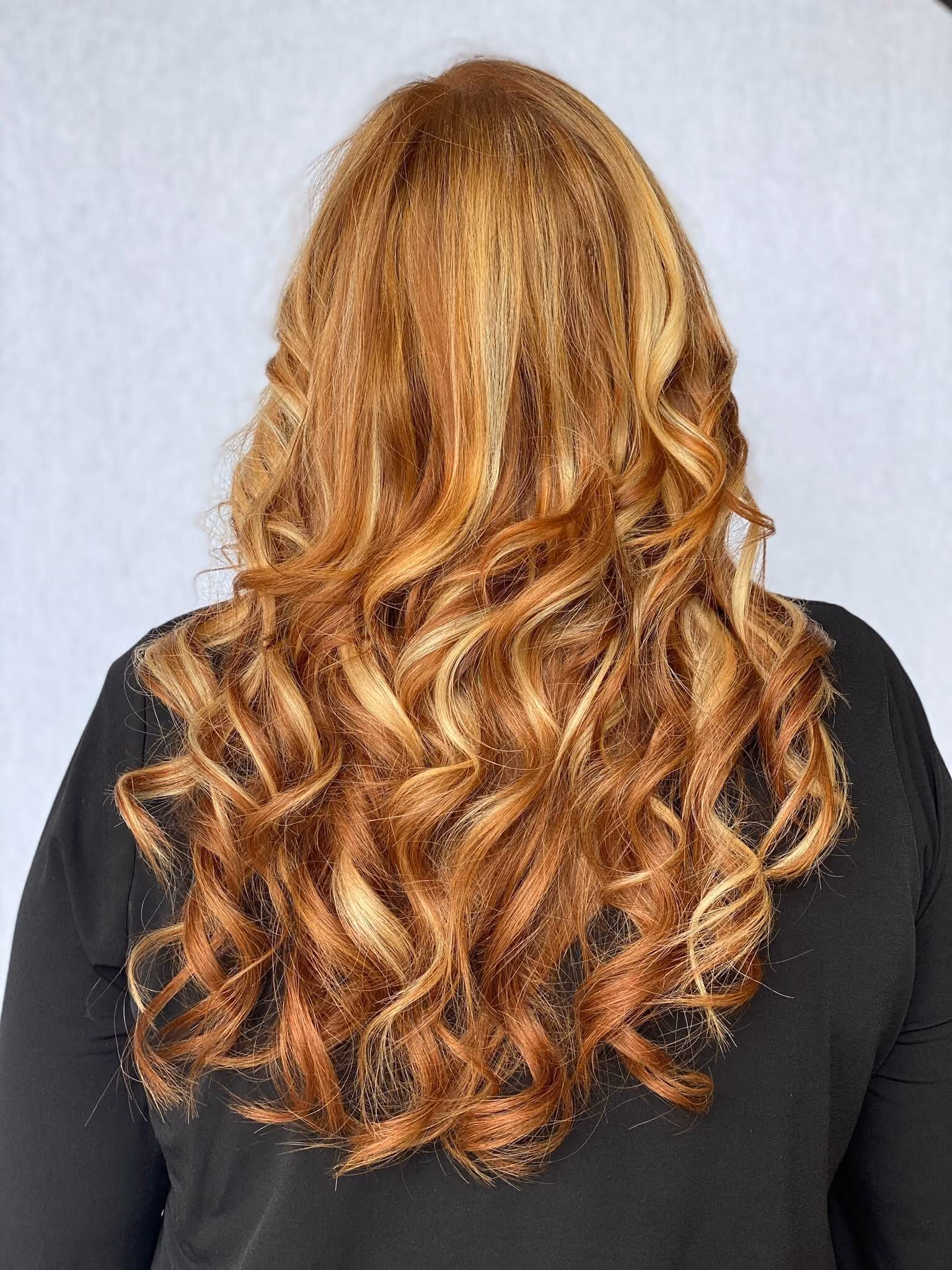 Long copper red hair with golden blonde highlights in bouncy curls after hair extensions at Janelle Alexis Salon in Houston