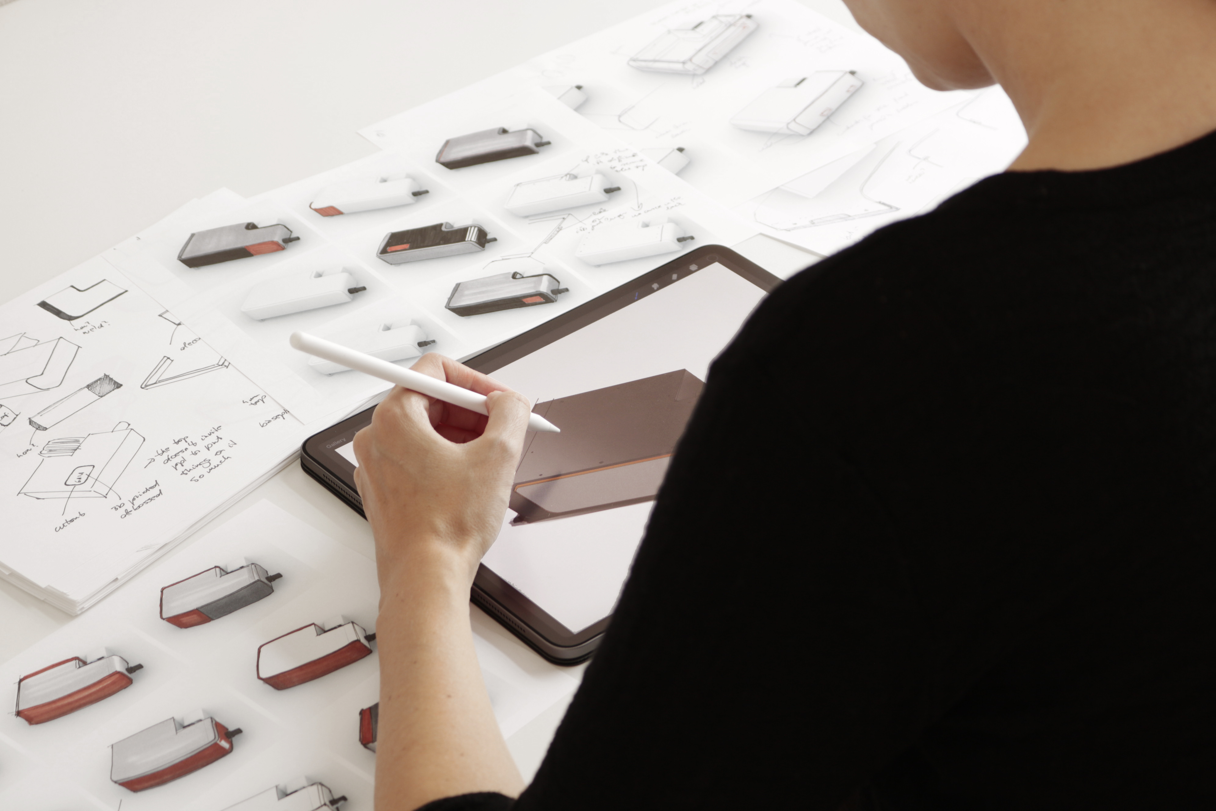 Female industrial designer sketching on an iPad with hand-drawn sketches around.