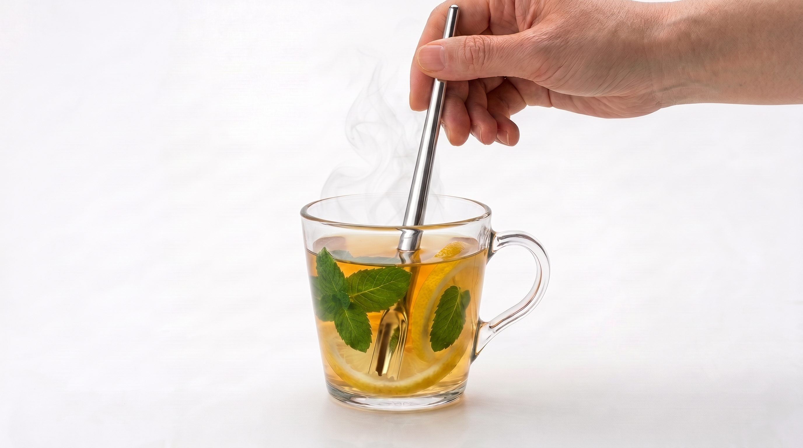 A hand holding a tea and cocktail stirrer in a cup of hot tea with lemon.