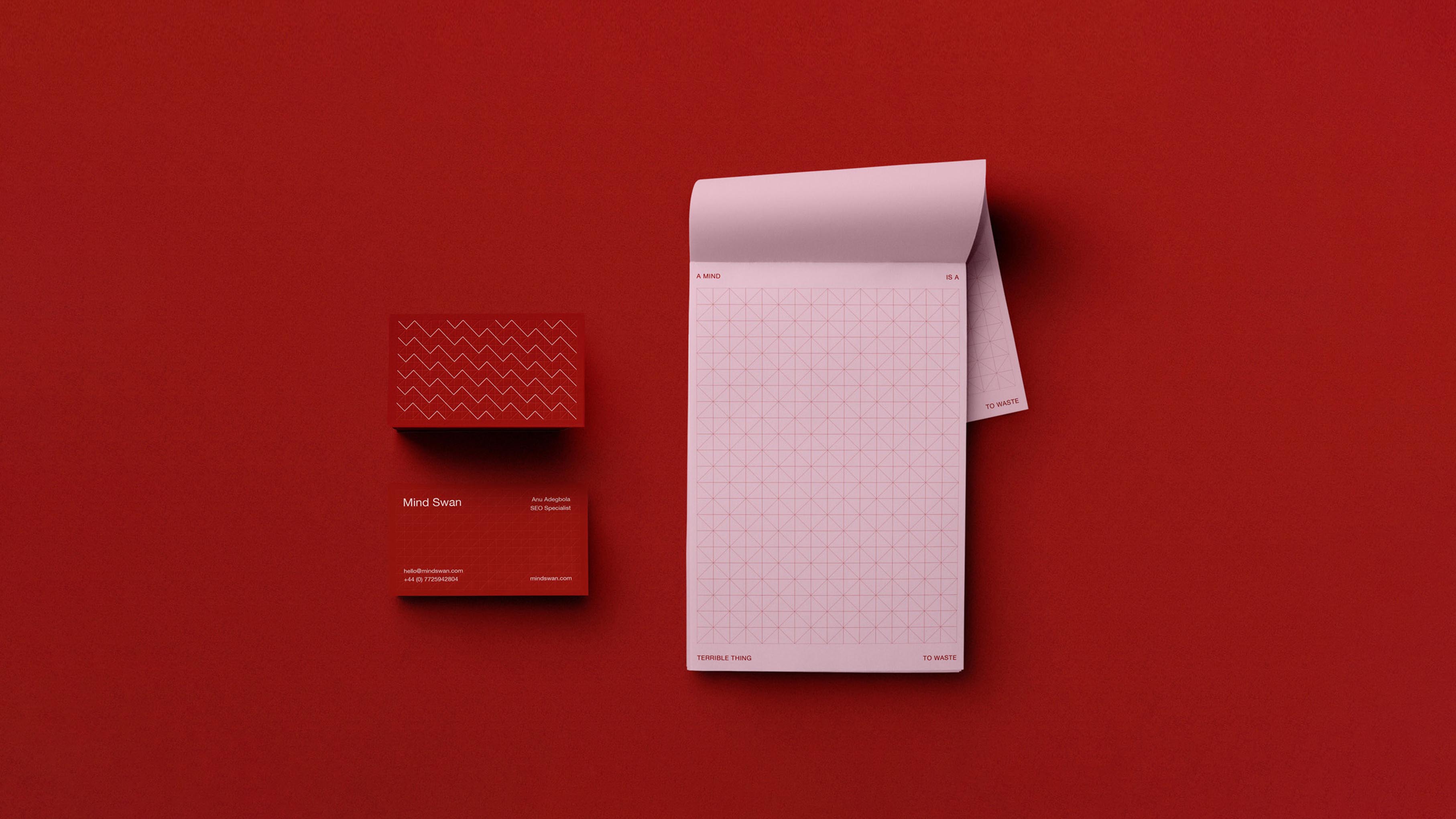 Pink notepad with geometric grid pattern and partial text beside two red business cards on a red surface.
