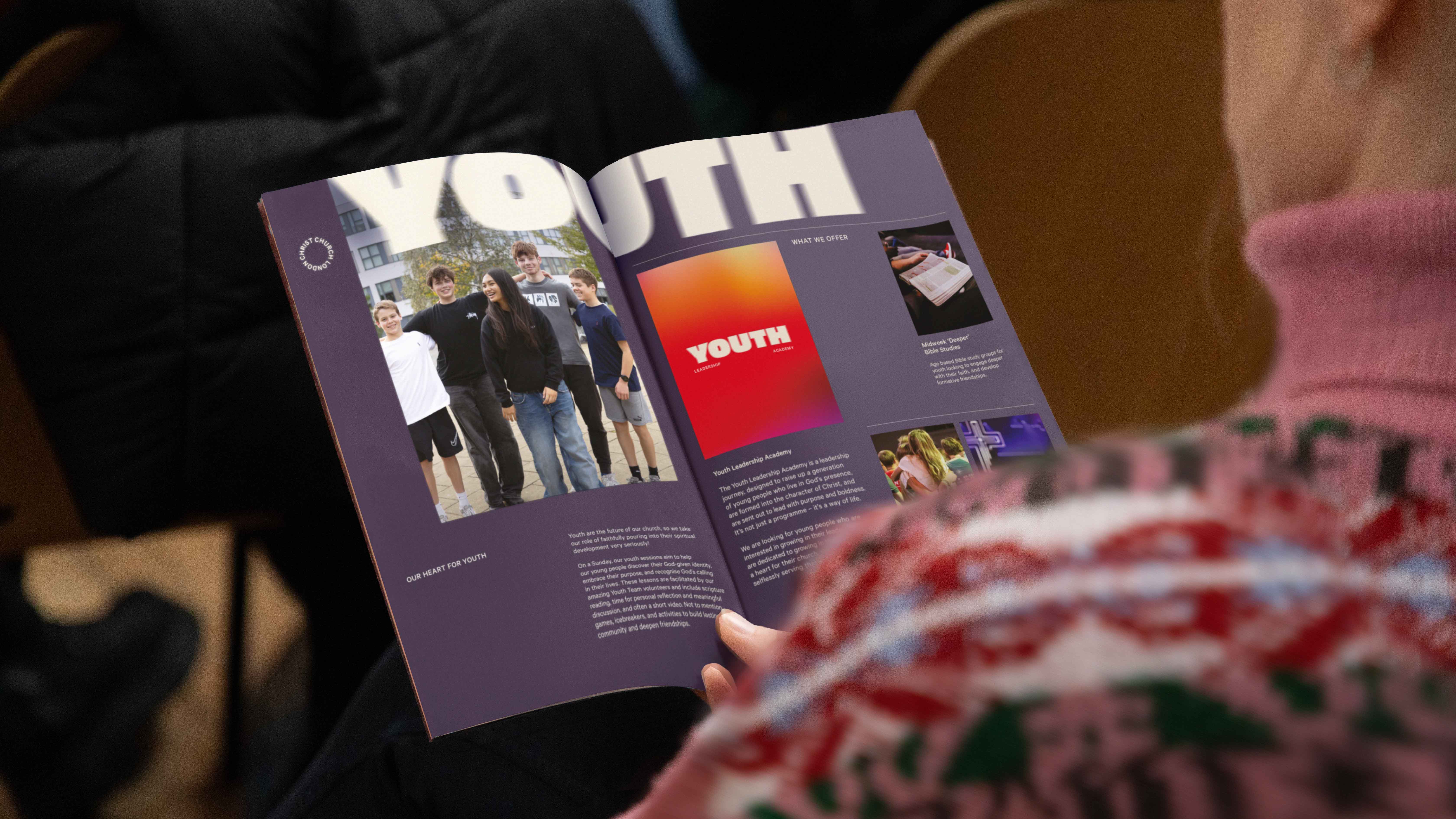 Person holding an open booklet with a purple background featuring a group photo of teenagers and text about youth programs.