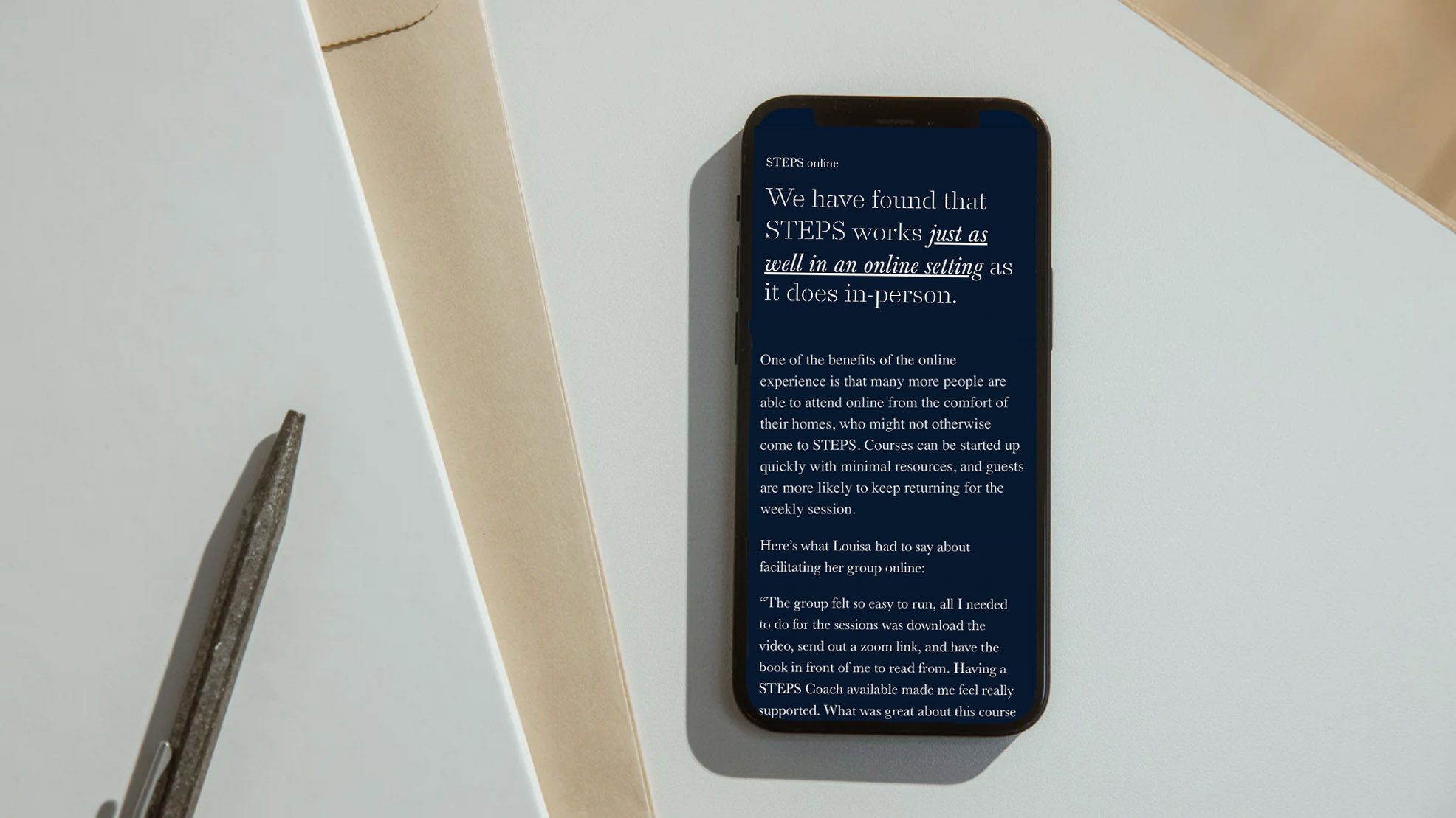 Smartphone on a desk displaying text about STEPS online working as well as in-person.