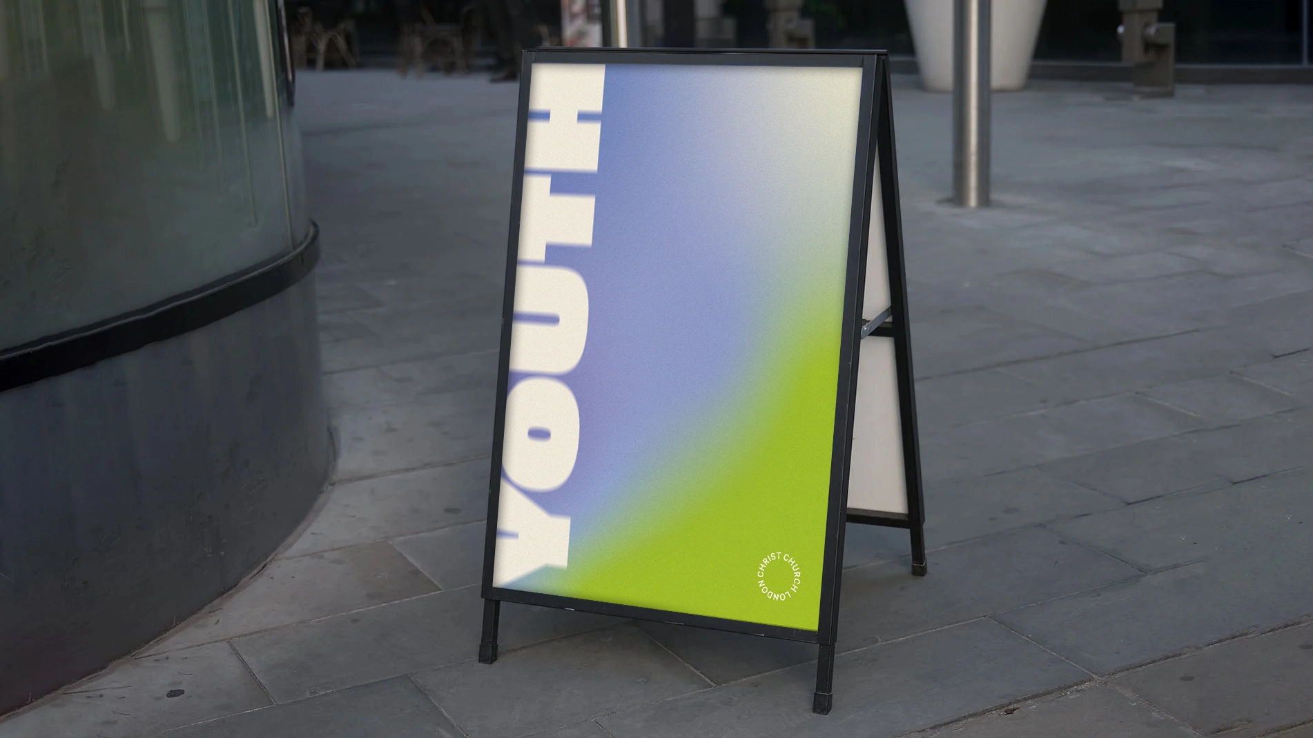 Sidewalk sandwich board sign with gradient blue and green background and partial white text 'YOUTH'.