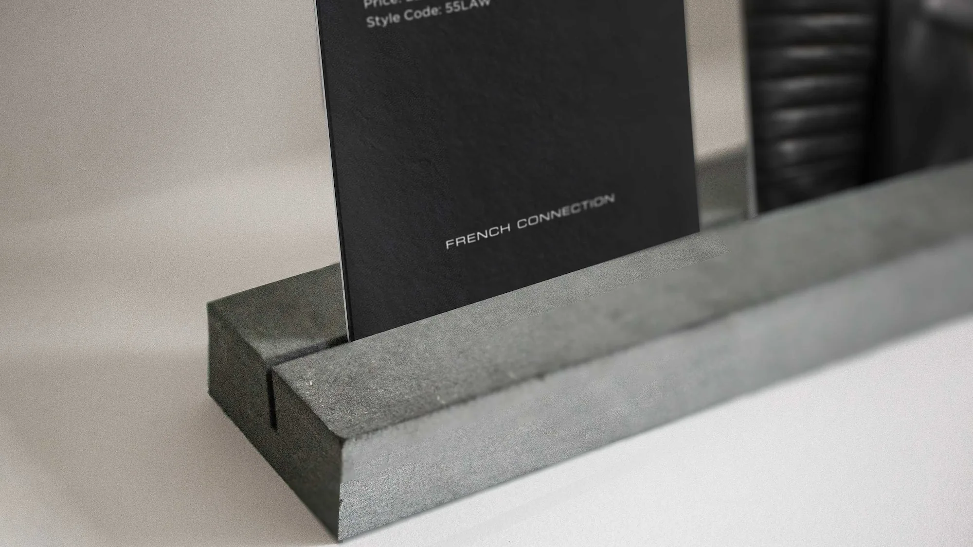 Black French Connection card held upright in a textured gray concrete holder on a light gray surface.