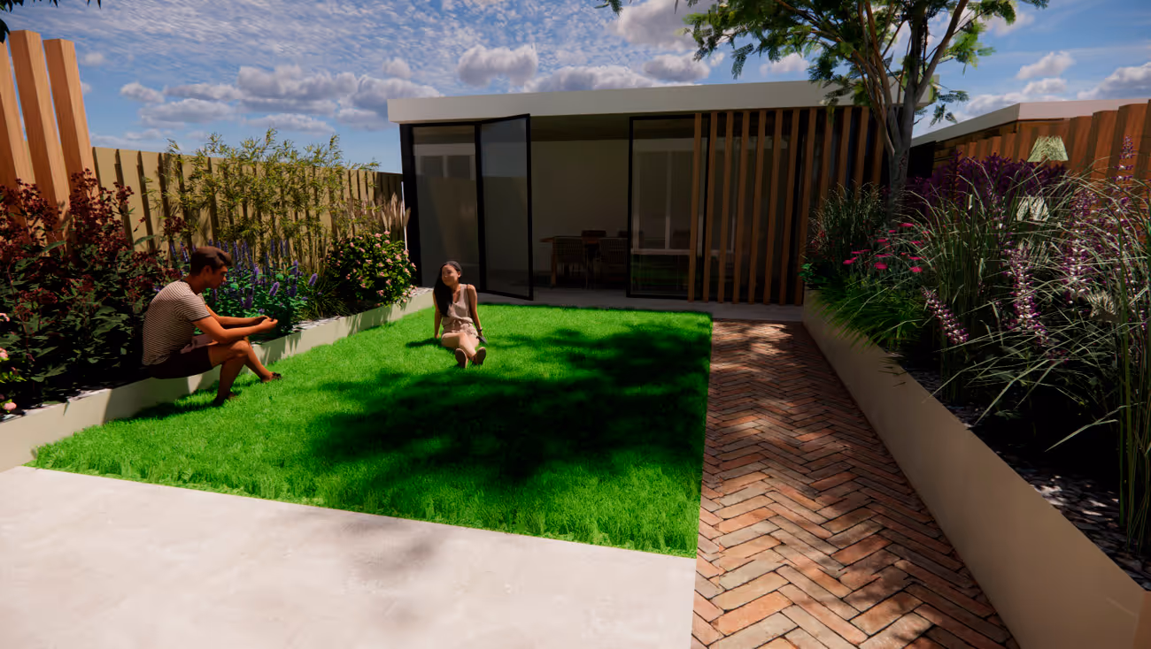Two people sitting and relaxing on a vibrant green lawn in a modern backyard with landscaped flower beds, a brick pathway, and a building with glass doors.