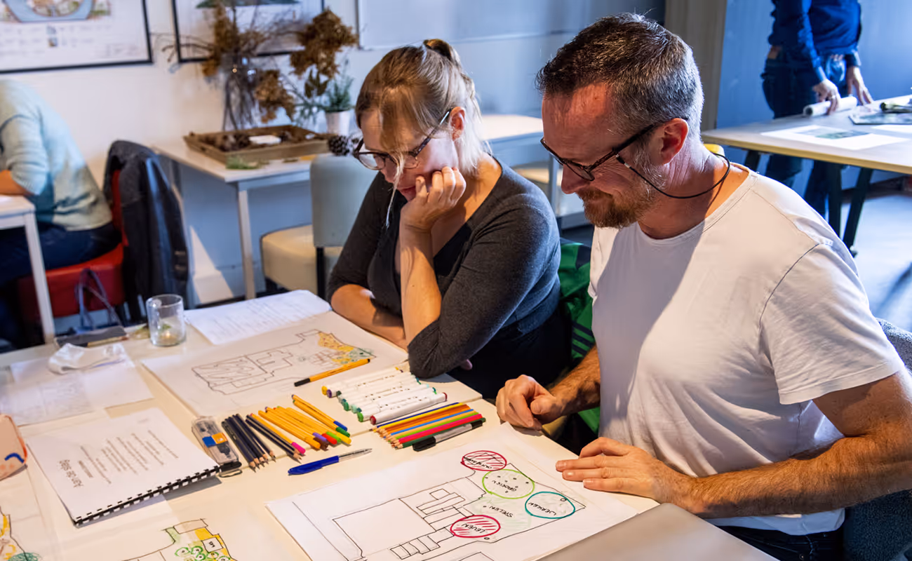 Man and woman sitting at a table coloring architectural-style drawings with colored pencils and markers.