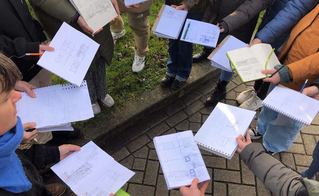 Group of people standing in a circle outdoors, holding notebooks and sketchpads with architectural drawings.