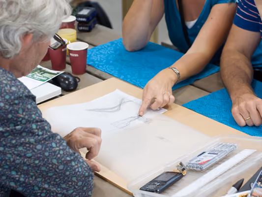 Three people sitting at a table reviewing and discussing architectural sketches and drawings.