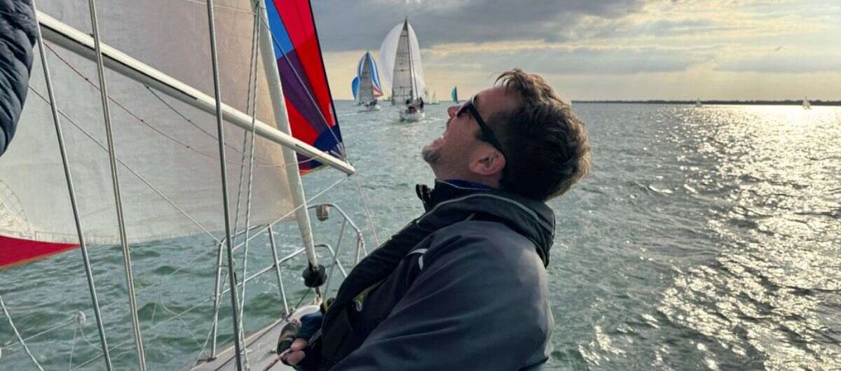 A man trimming a boat spinnaker at sea.