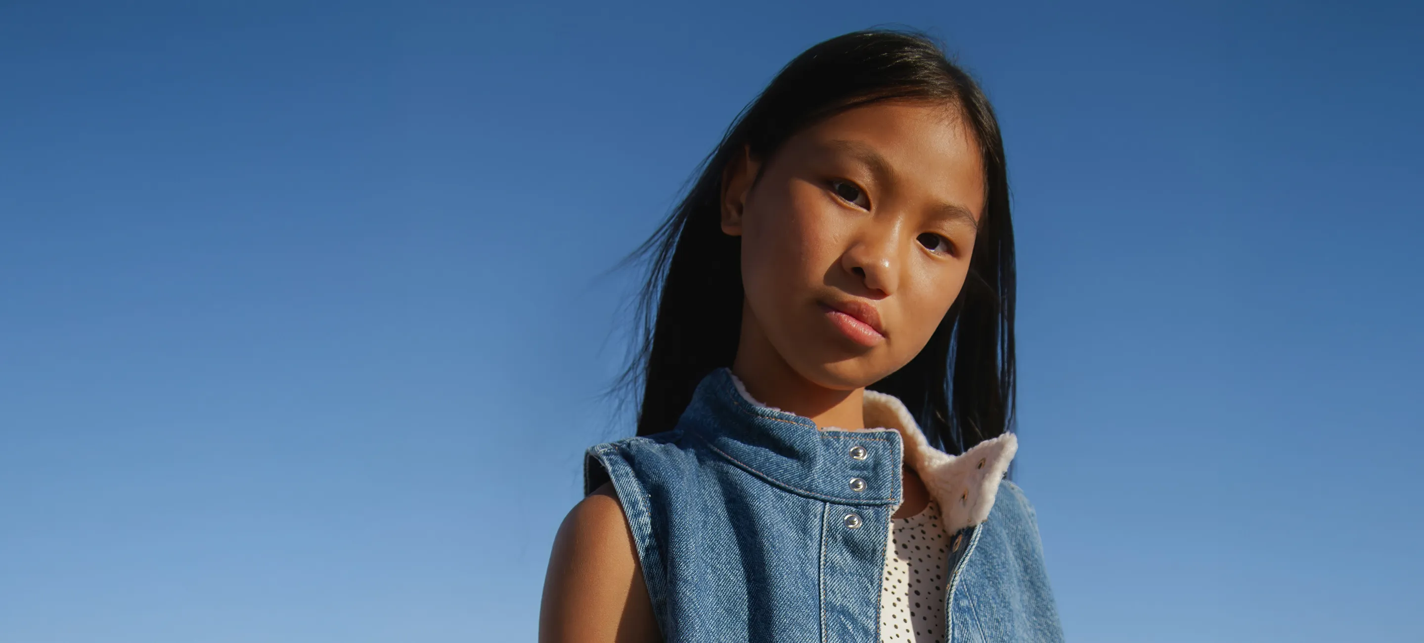 A young girl in a denim vest is posing for a picture.