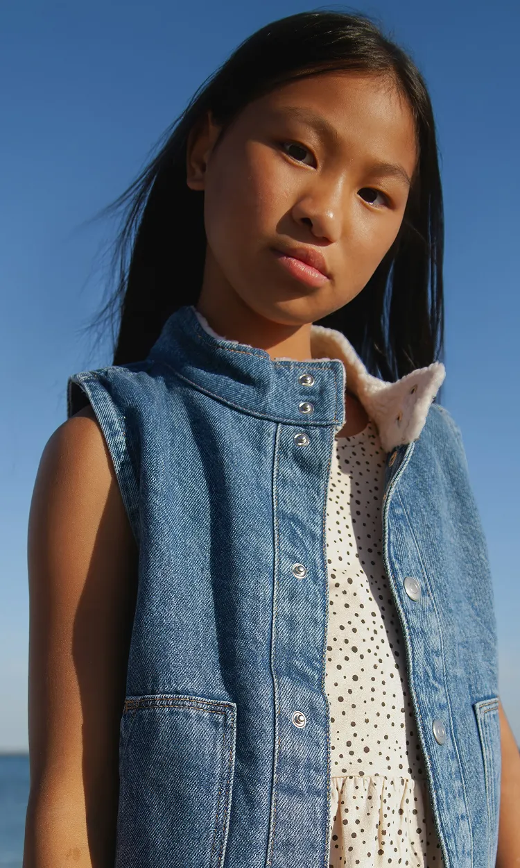 A girl in a white dress and a denim vest.