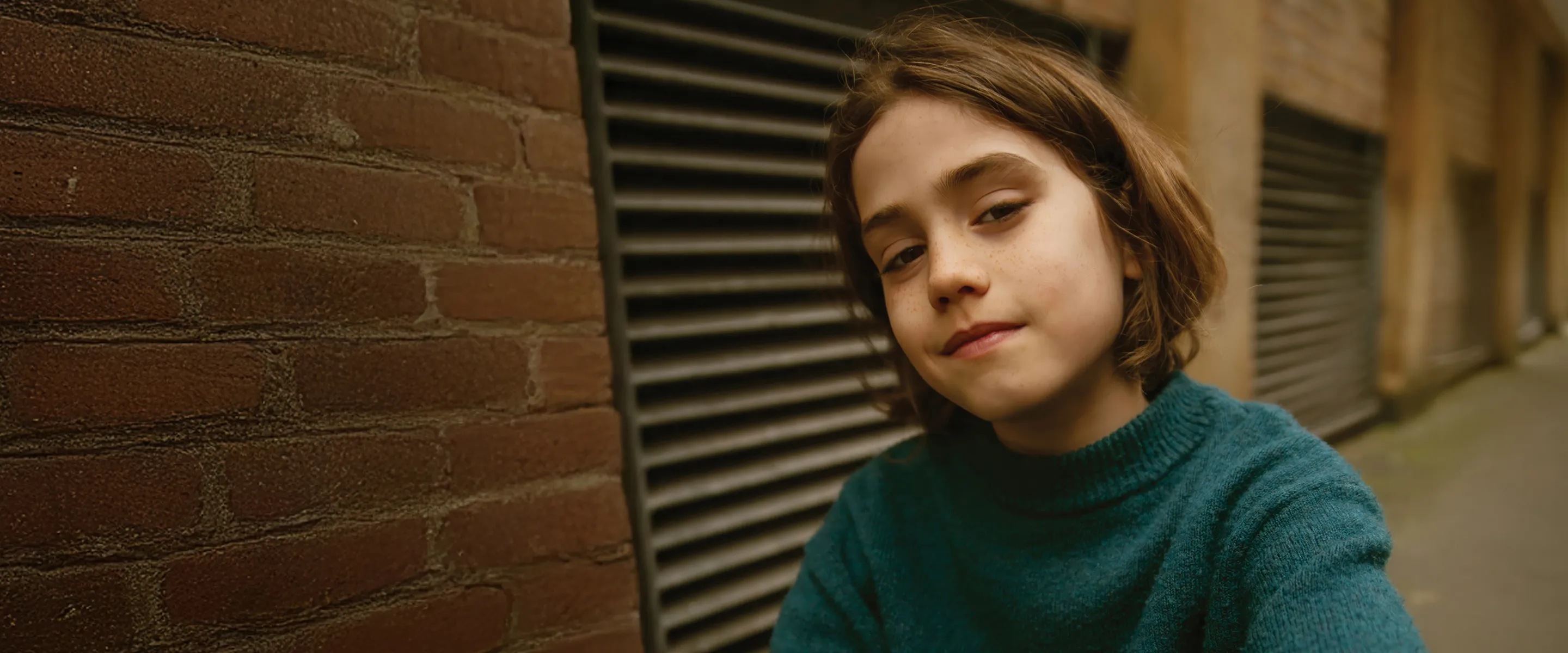 A young girl leaning against a brick wall.