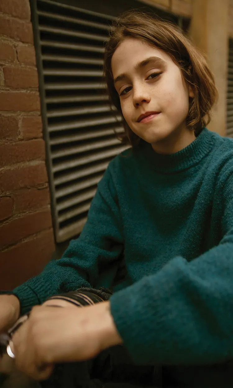 A young girl leaning against a brick wall.