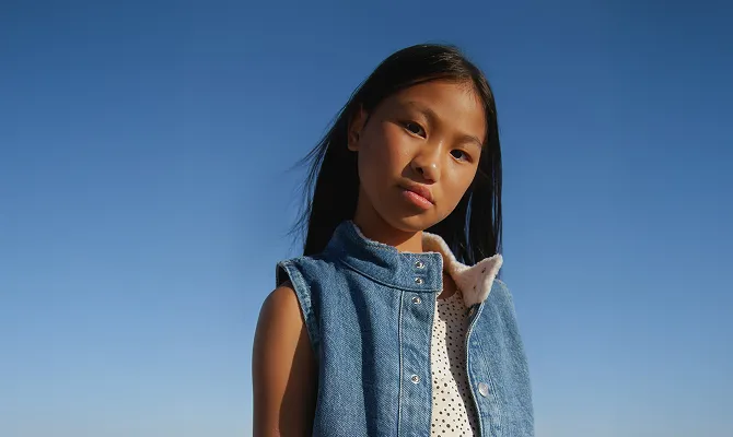 A young girl wearing a denim vest and polka dot shirt.