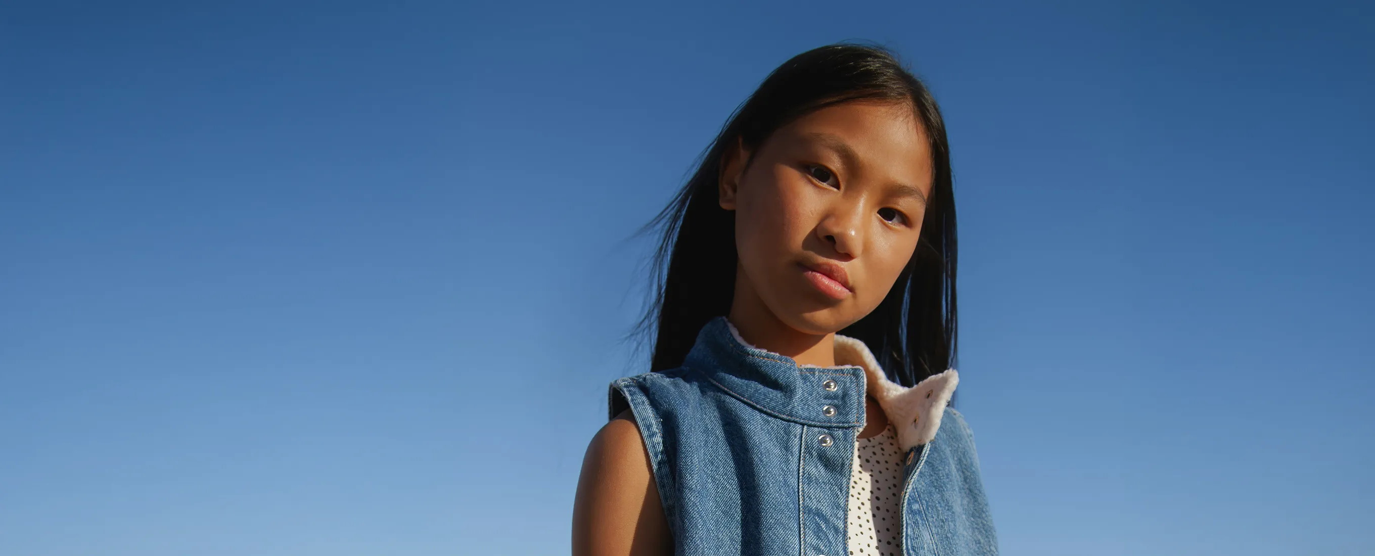 A young girl in a denim vest and tie.