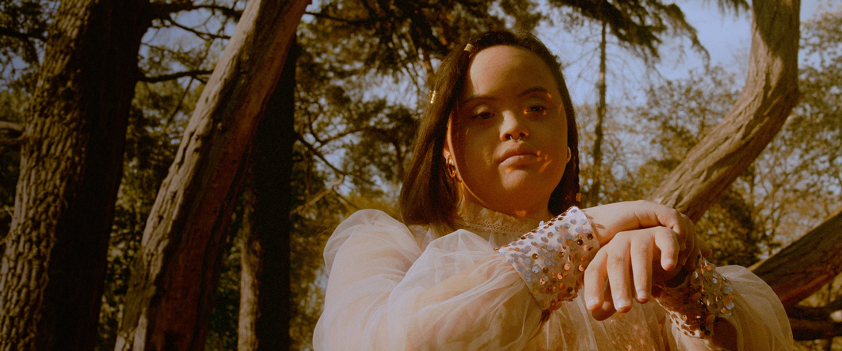 Person with Down syndrome wearing a sheer top with sequined cuffs in an outdoor wooded setting.
