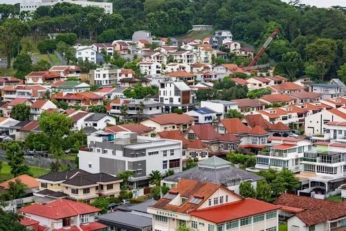 Dense residential area with houses featuring red and gray roofs surrounded by lush greenery and trees.