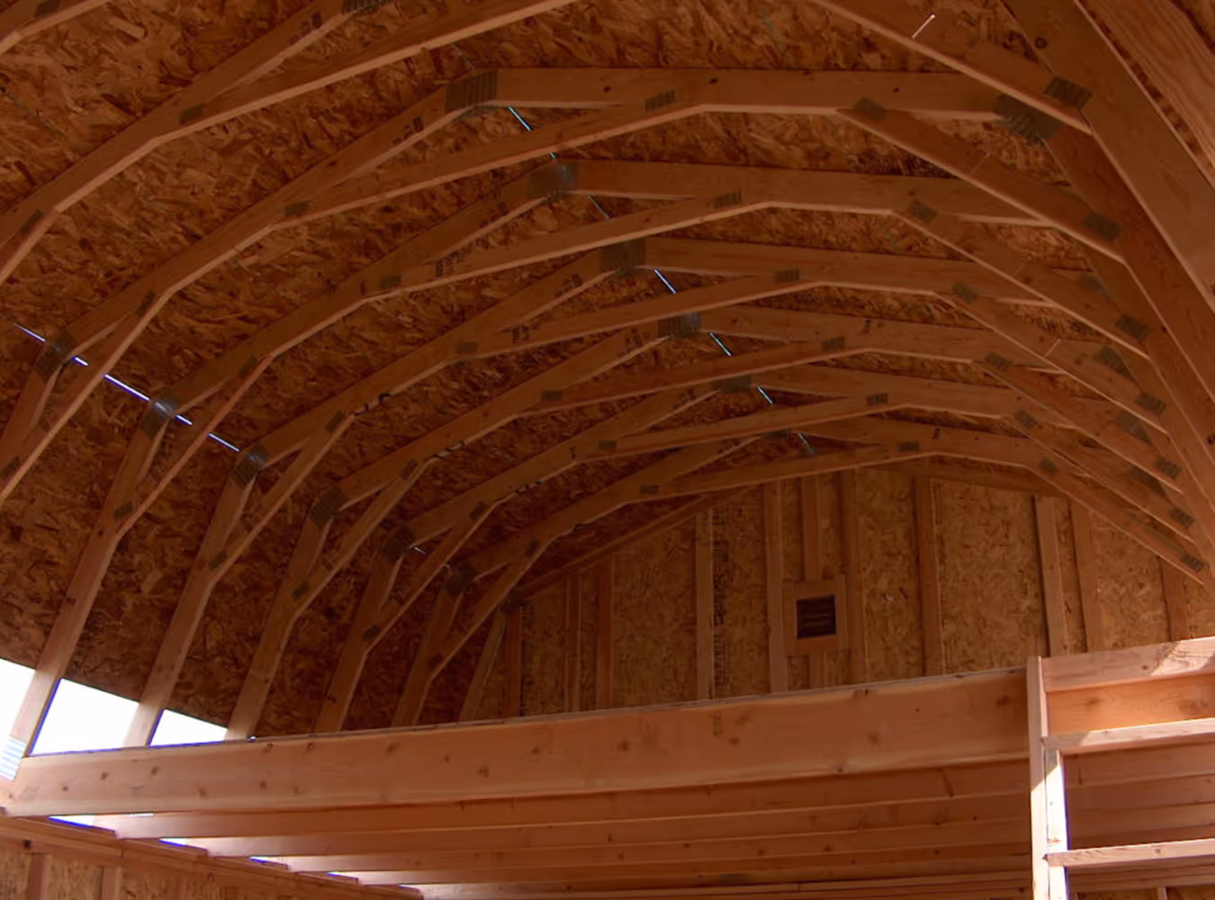 Interior of a wooden barn under construction with exposed rafters and framing.