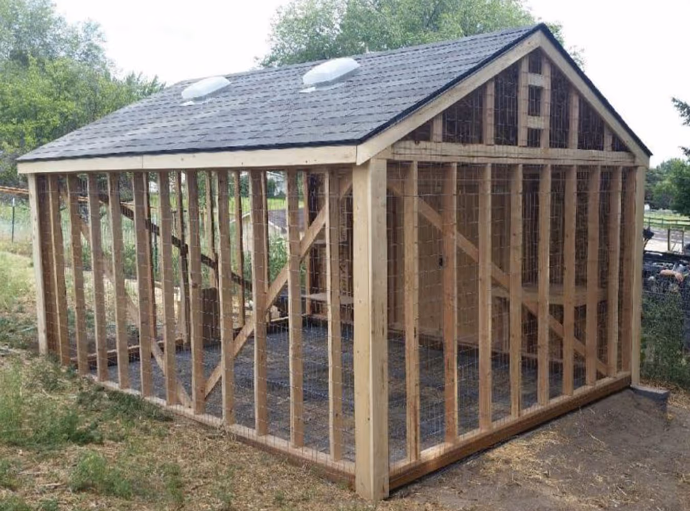 Wooden chicken coop with wire mesh sides and a shingled roof with two vent domes.