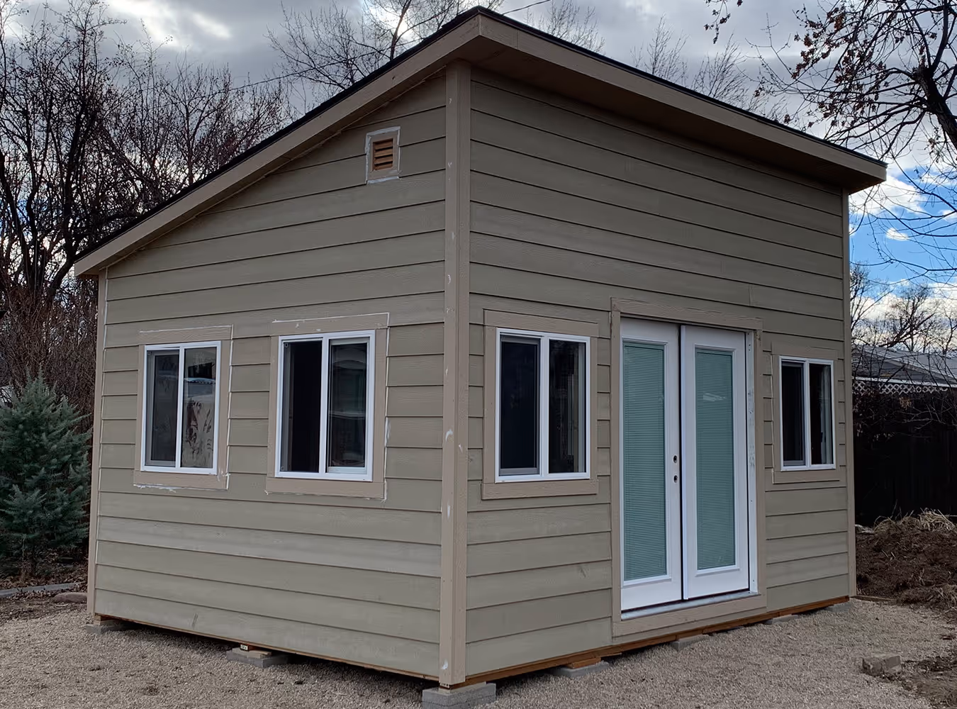 Newly built small beige shed or outbuilding with multiple windows and double doors with blinds.