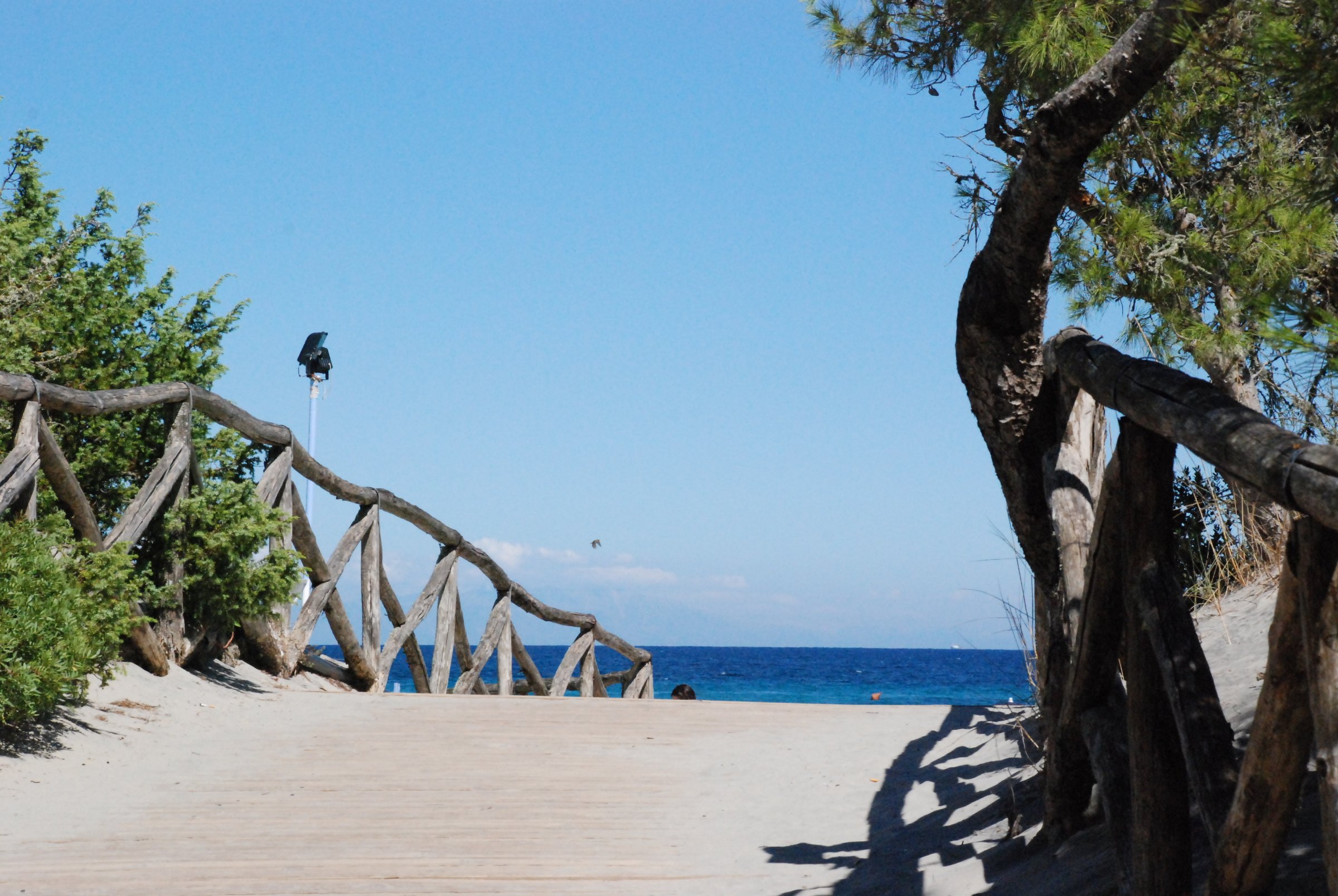 Sentier sablonneux avec clôture en bois menant à une plage du Salento