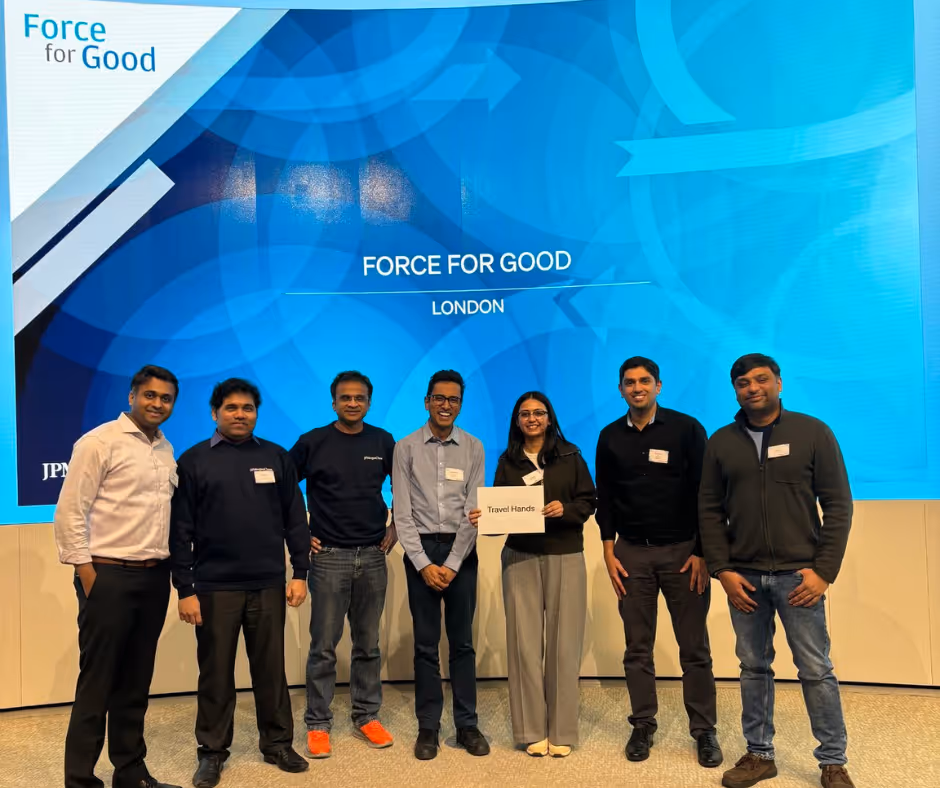 Travel Hands team with JP Morgan Chase volunteers during the Force for Good program in London. The group stands in front of a large blue backdrop displaying the words “Force for Good – London,” celebrating their collaboration to develop accessible technology for visually impaired people.