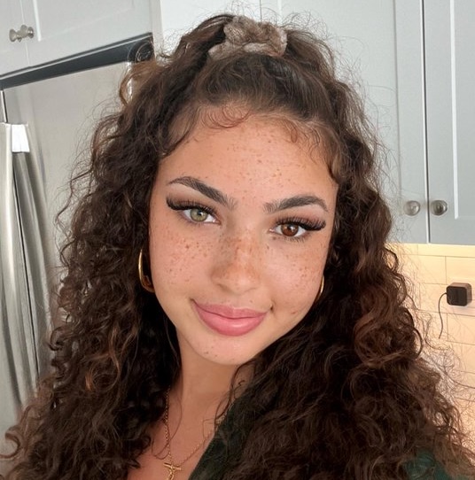 woman with dark hair smiling while looking off-camera in a patterned top against a light background