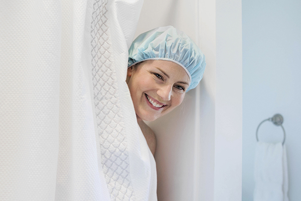 Woman peeking out from behind shower curtain wearing a shower cap
