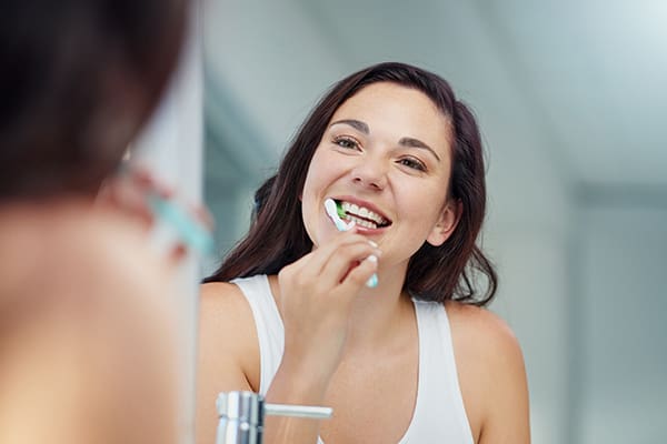 woman looking in mirror while brushing teeth