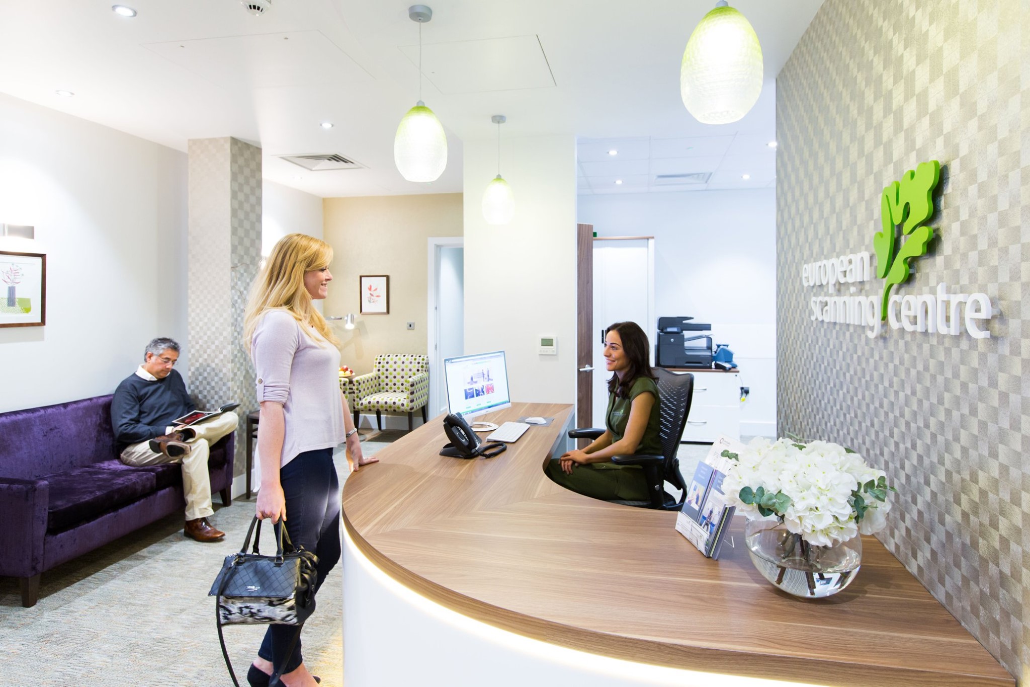 Patient greeted at reception desk by smiling member of staff