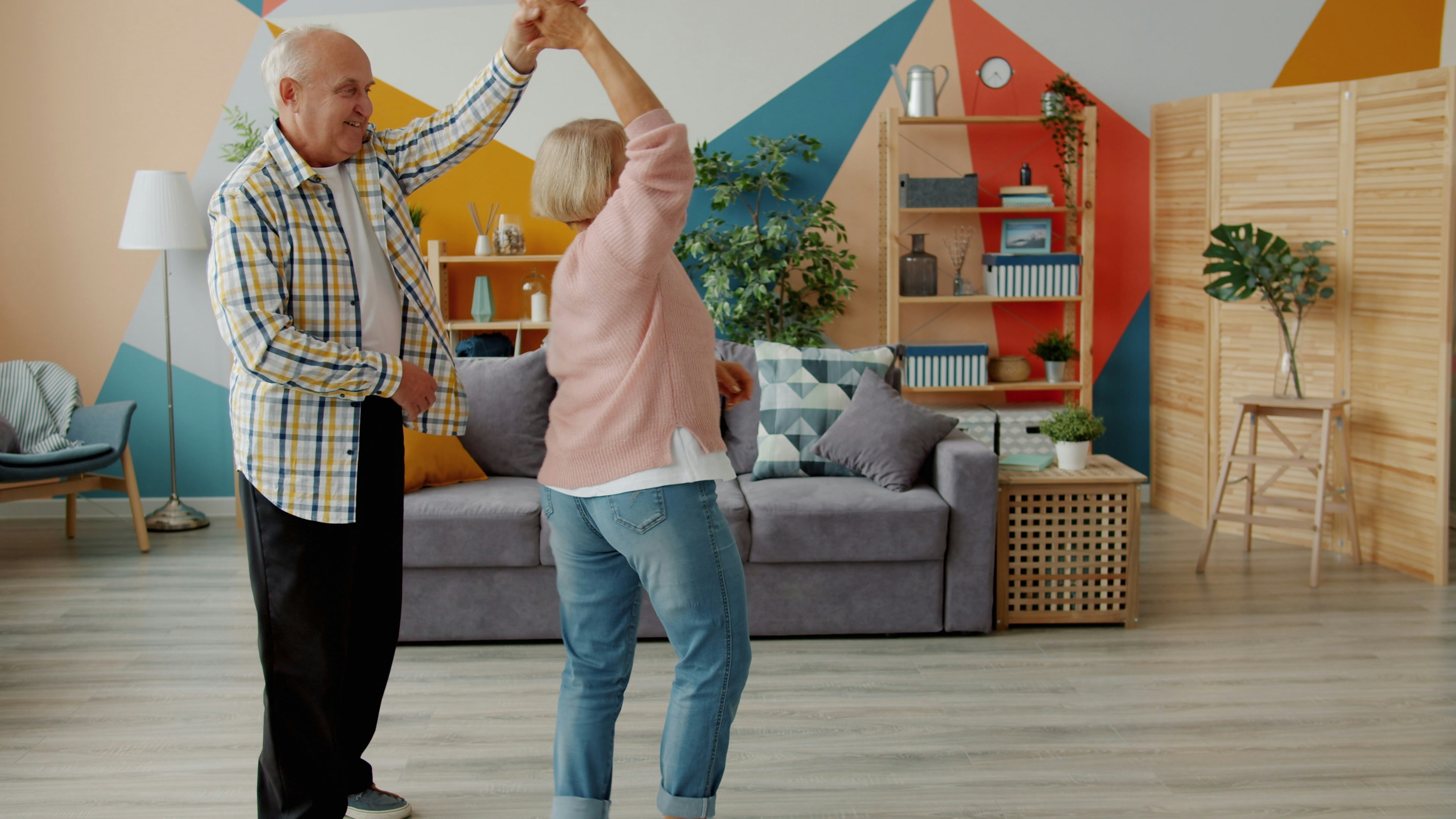 Two older adults dancing together in a brightly coloured room.