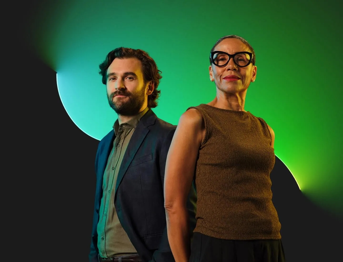 Two business professionals standing confidently against a dark background with green gradient lighting, representing leadership and executive roles.