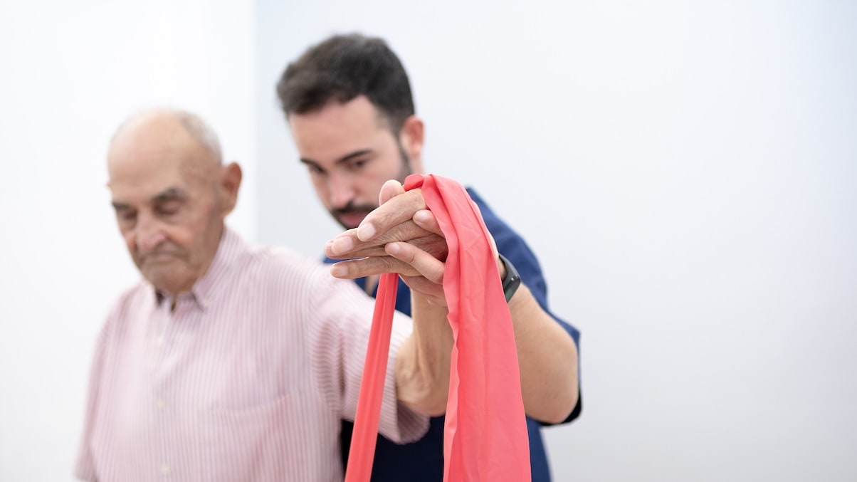 Fisioterapeuta acompañando ejercicio con banda elástica en sesión de fisioterapia geriátrica