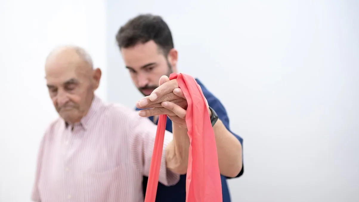 Fisioterapeuta acompañando ejercicio con banda elástica en sesión de fisioterapia geriátrica