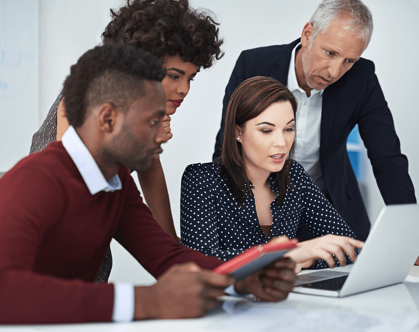 Diverse group of four business colleagues looking at a laptop screen together in an office setting.