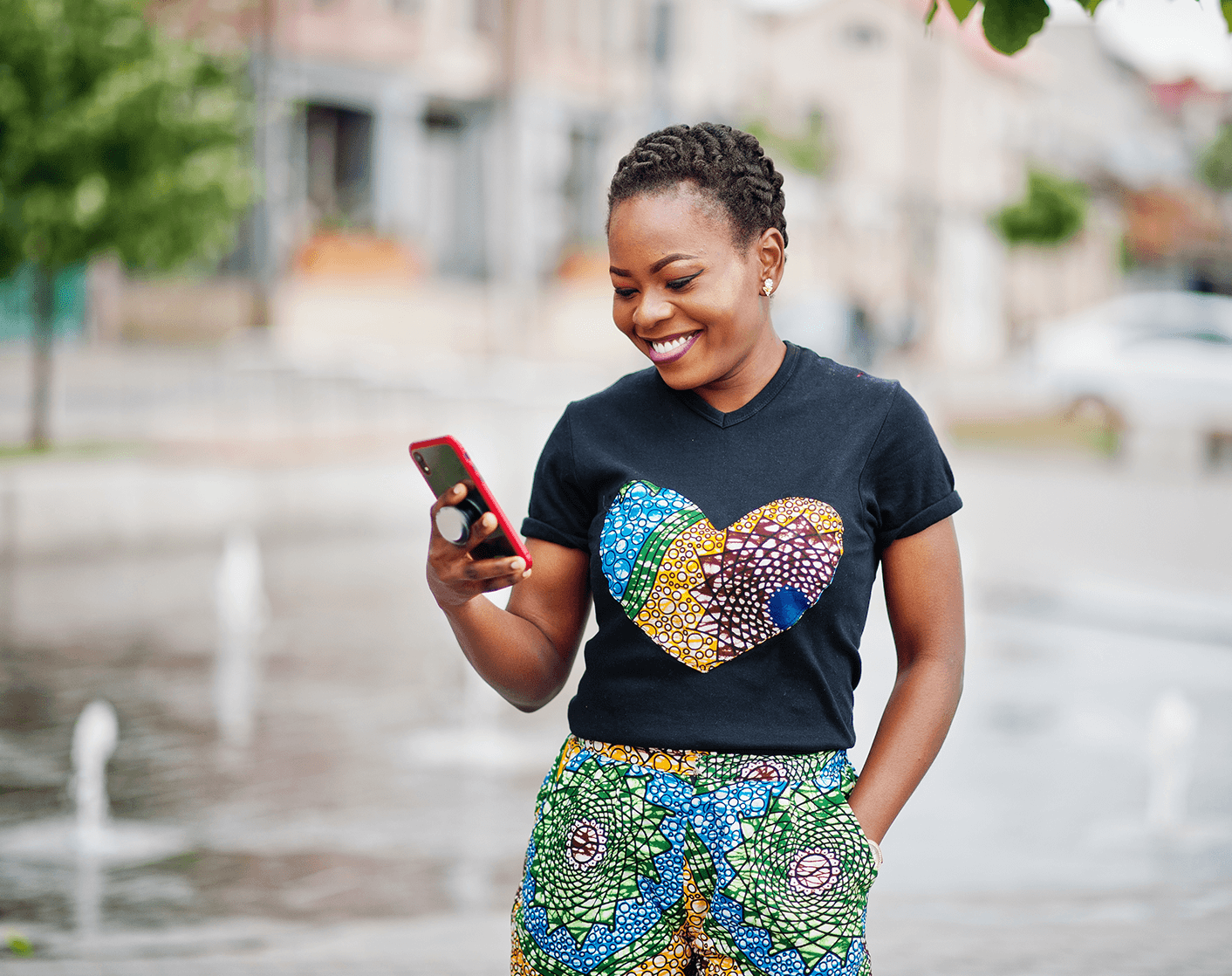 Smiling woman outdoors looking down at her mobile phone, wearing a patterned heart t-shirt.