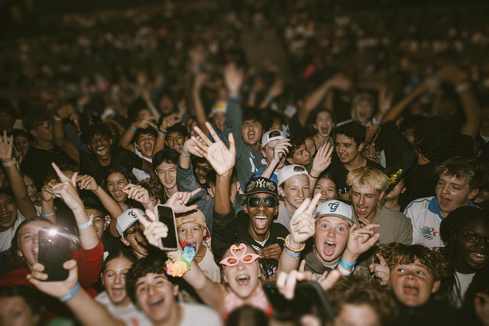 Excited diverse crowd of young people cheering and raising hands at a lively event.