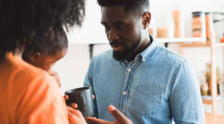 man in blue shirt holding a cup speaks with a mother holding a child