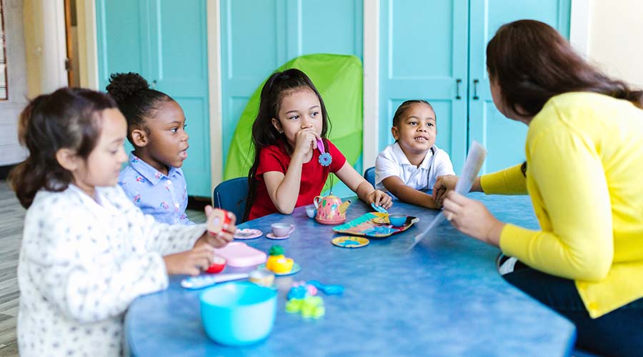teacher playing with 4 kids on a table with blue cover