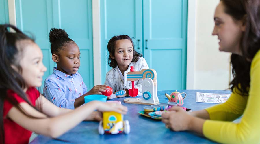 teacher playing with kids on a table with blue furniture visible in the background