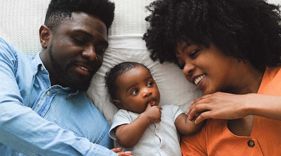 Two parents lay down with their baby and speak to the child.