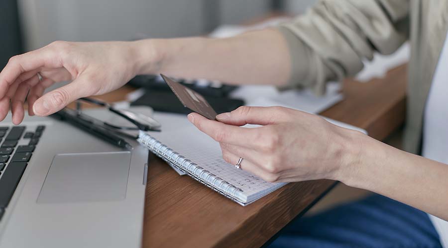 A woman holds a credit card, as she sits in tront of a computer.