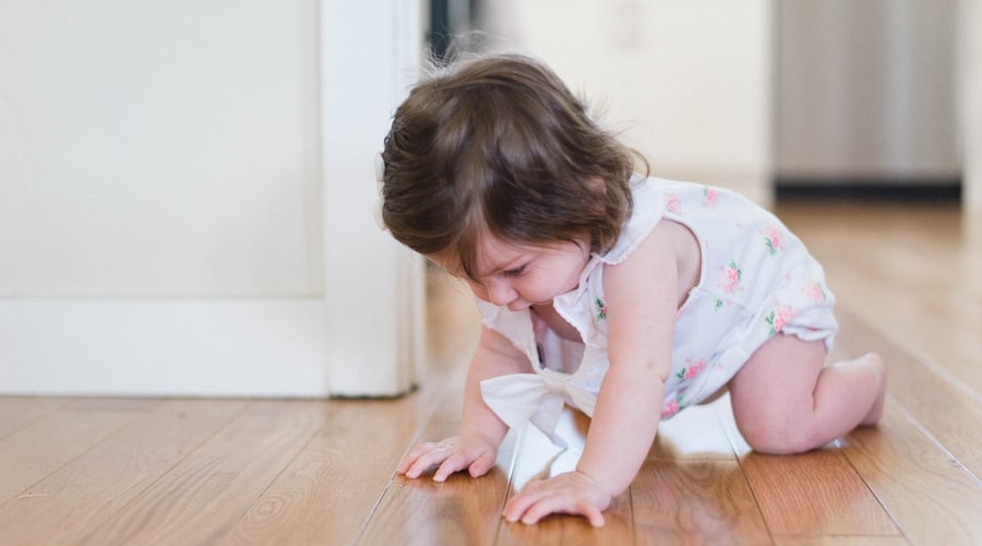 A young toddler crawls across the floor of a nursery room.