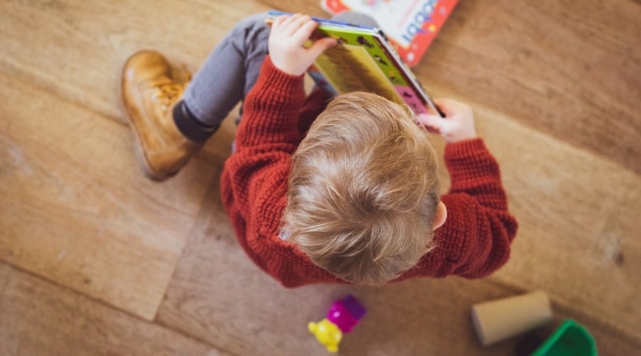 An early years child explores a book in a nursery setting's book corner.