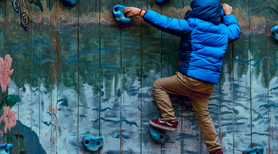 An early yeas child climbs up an outdoor climbing wall, at an early years setting.