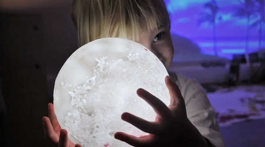 A photograph of a pre-schooler at Little Barn Owls nursery exploring a lamp shaped like the moon