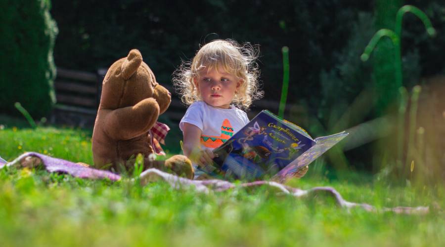 Girl holding a fairy-tail book while sitting on a blanket in a garden